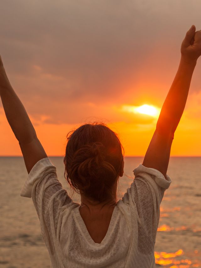 woman with her arms up in the air in front of the sunset
