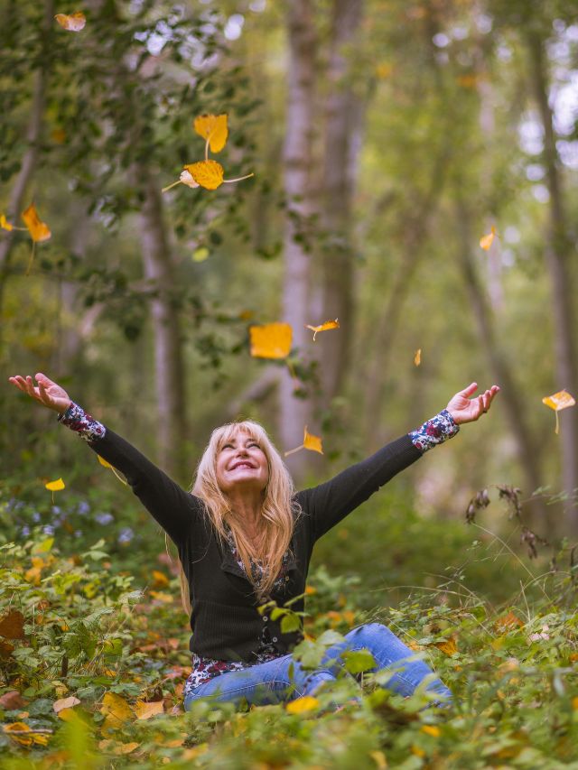 happy woman in the forest throwing leaves in the air