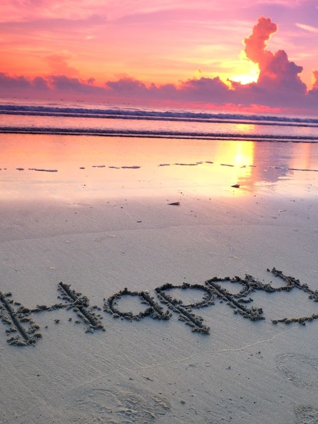 the word happy written in the sand in front of sunset