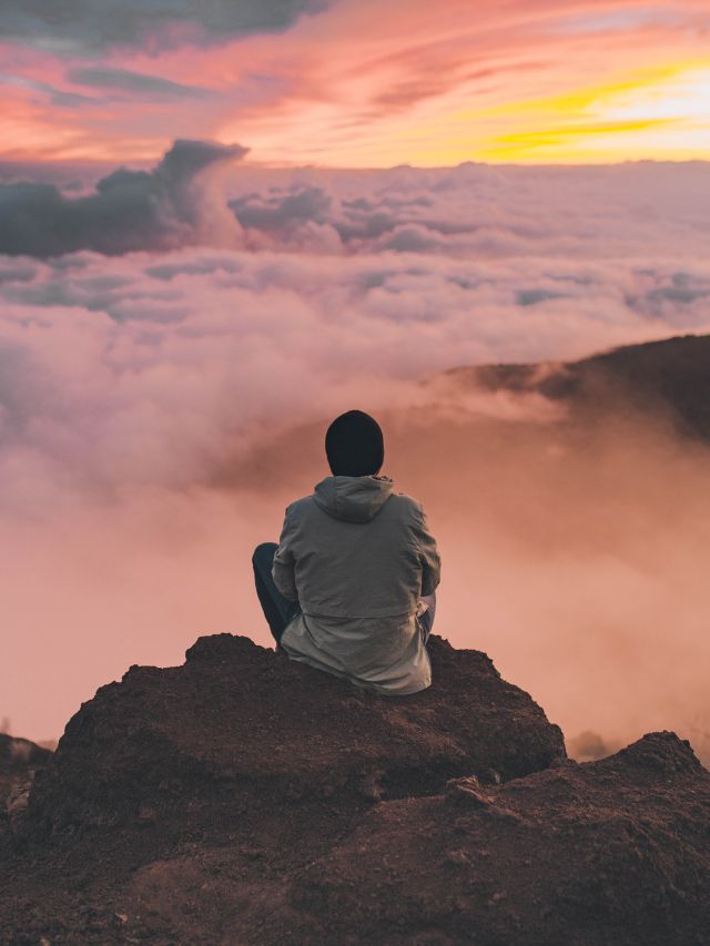 man sitting on rock with clouds