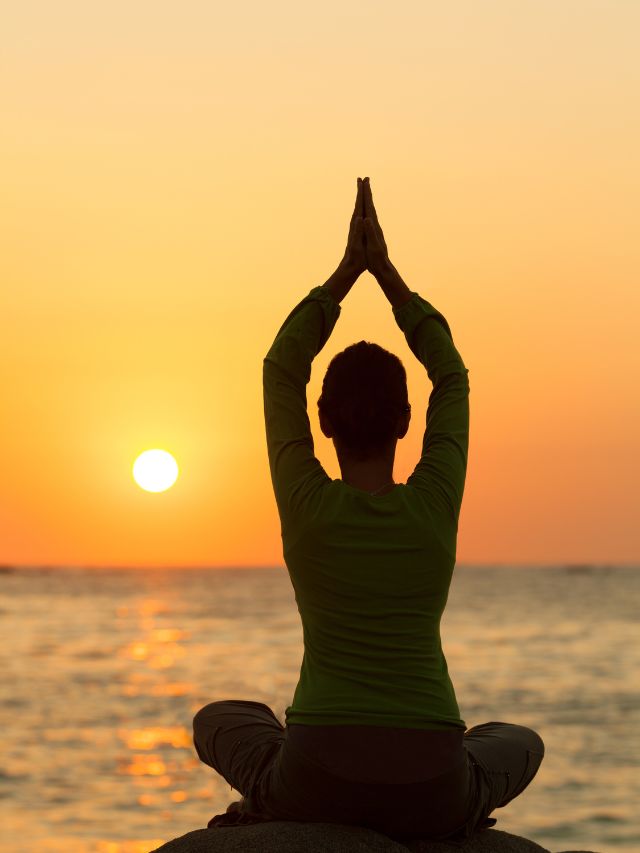 a woman meditating at sunset on the beach