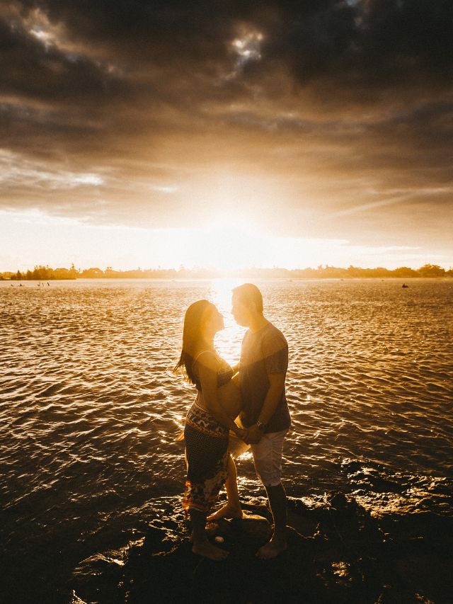 a couple looking at one another standing on a rock in the water