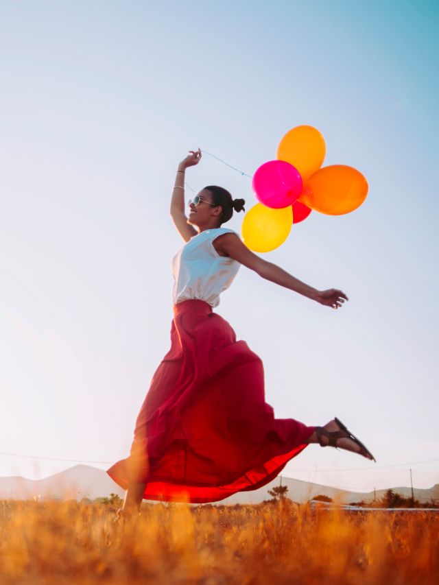 happy woman running in a field enjoying nature holding balloons