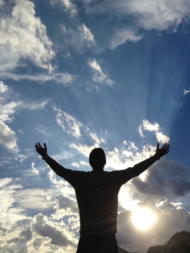 man with his arms open in front of light shining through the clouds