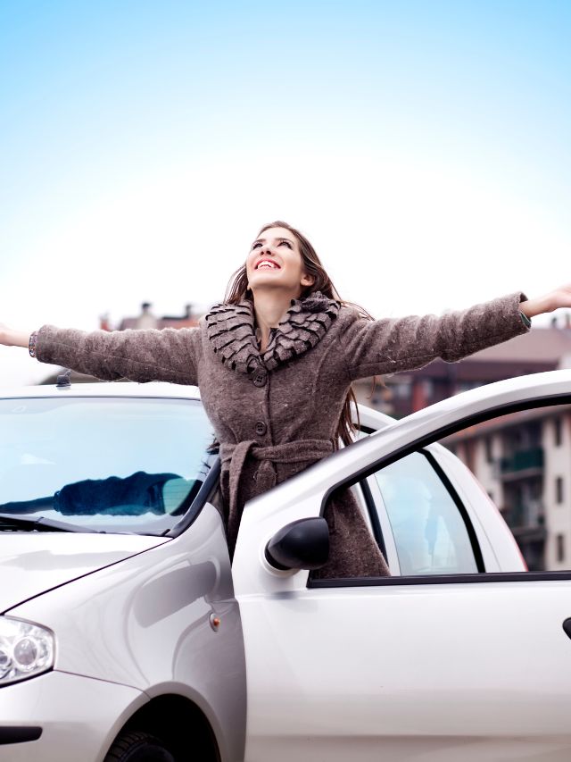 woman standing next to her car with her arms raised