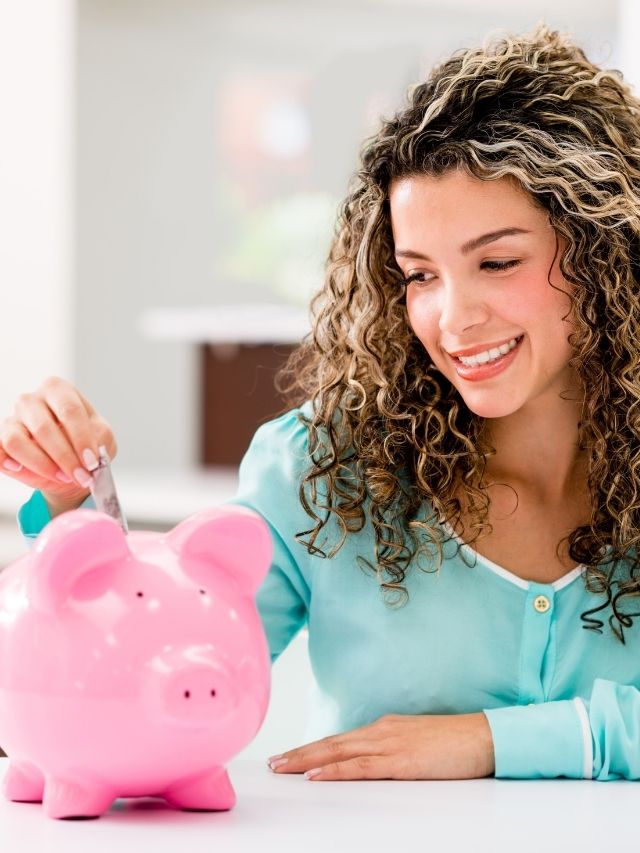 woman with curly hair putting cash into a pink piggy bank