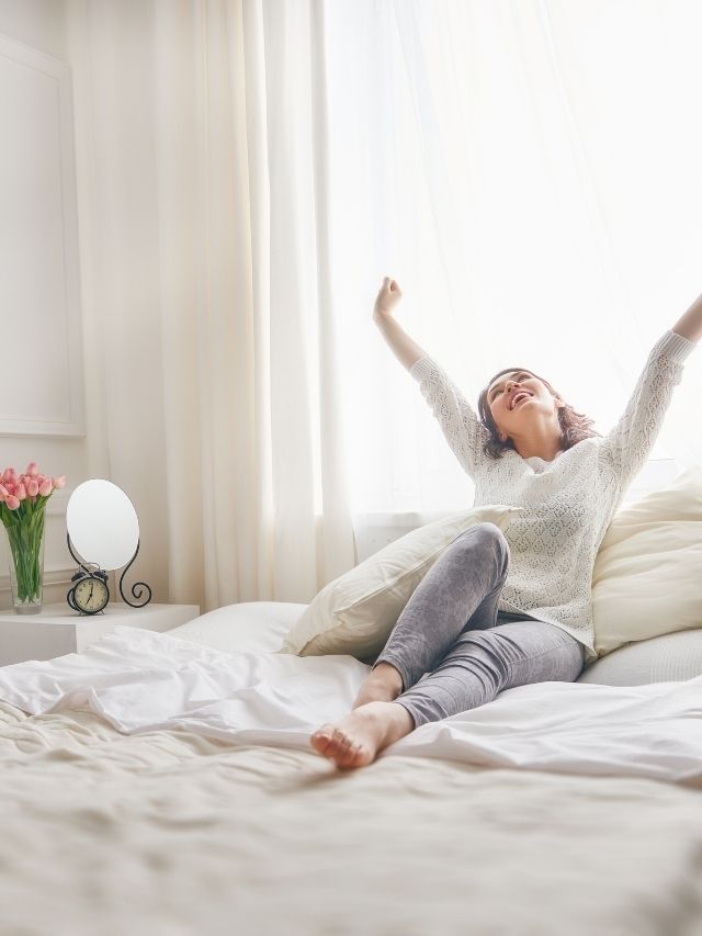 woman sitting on her bed stretching