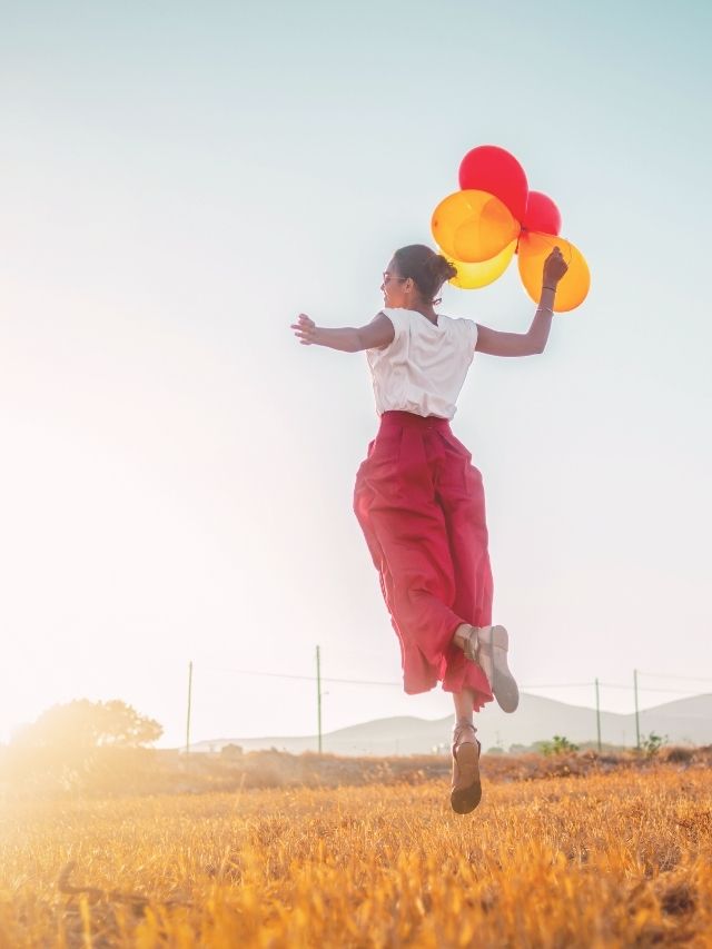 girl jumping up in the air holding balloons