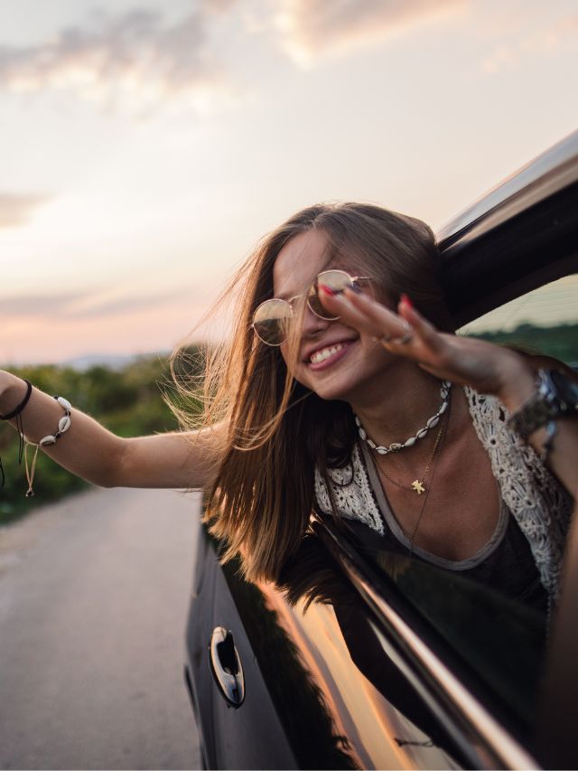 smiling woman hanging out car window