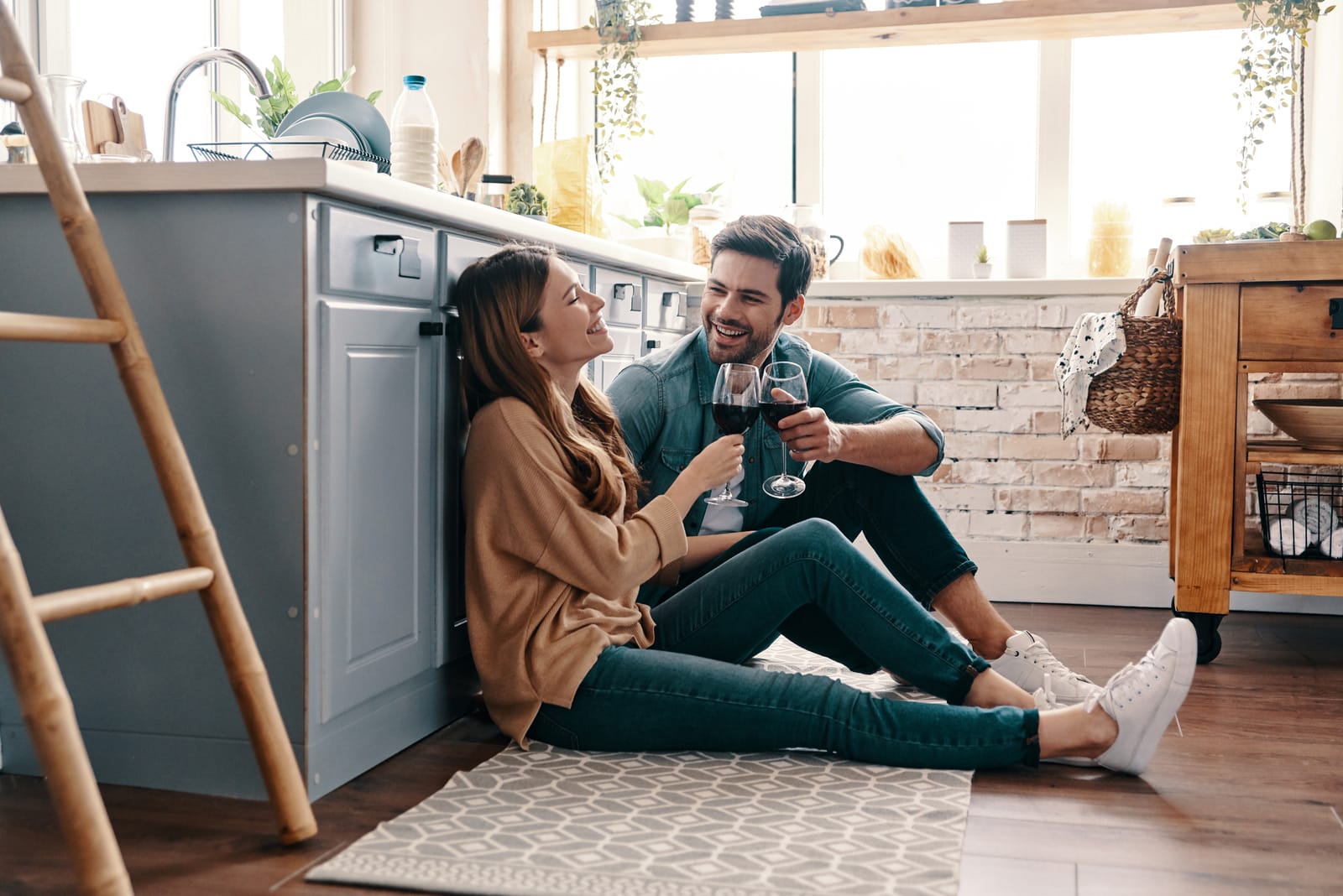a smiling couple on the kitchen floor sitting and drinking wine