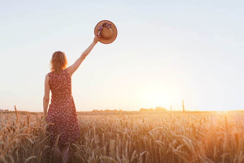 woman raises her hat at field