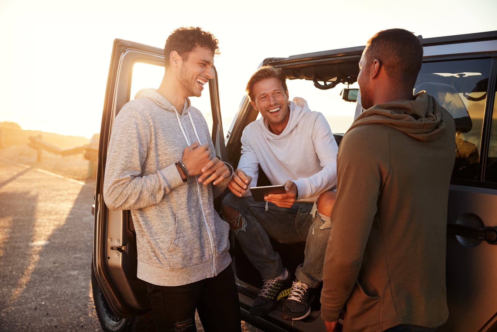a man stands with friends next to a car and laughs
