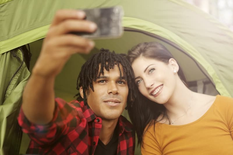 man and woman taking selfies near a camping tent