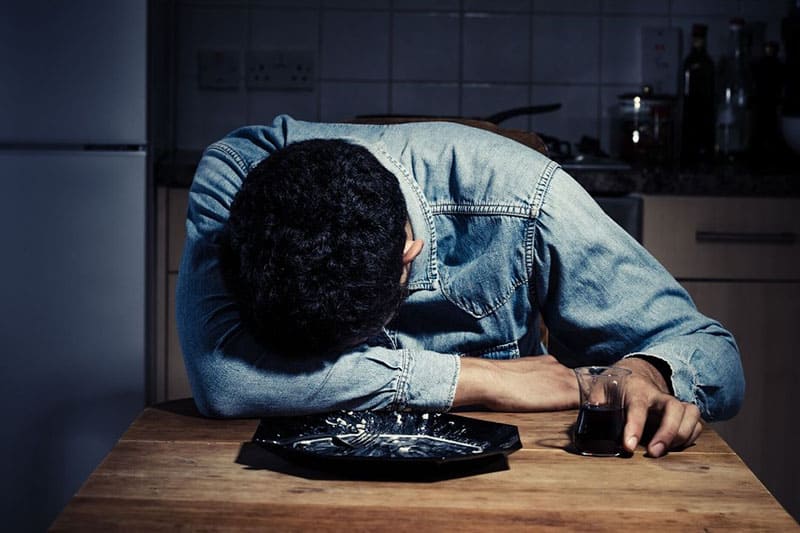 sad man sleeping with head on the table with wine on hand