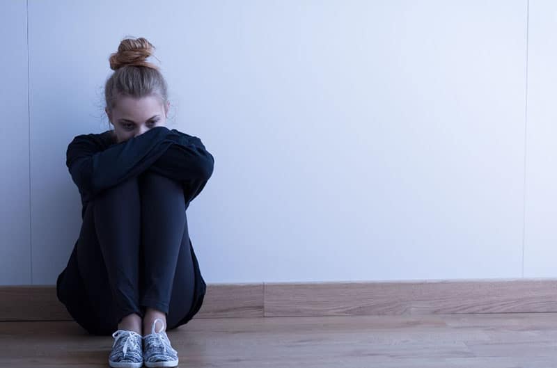 woman in black suit sitting on the floor leaning on white wall