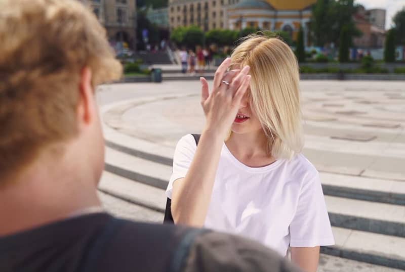 hand covering the face of the woman wearing white top facing a guy