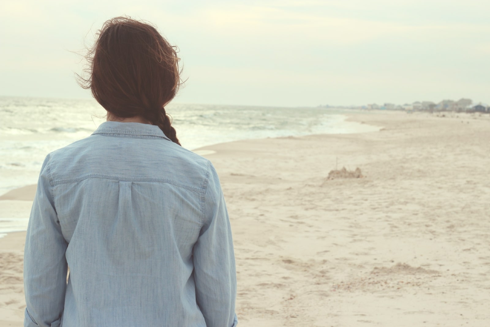 woman in denim shirt standing on shore looking at ocean