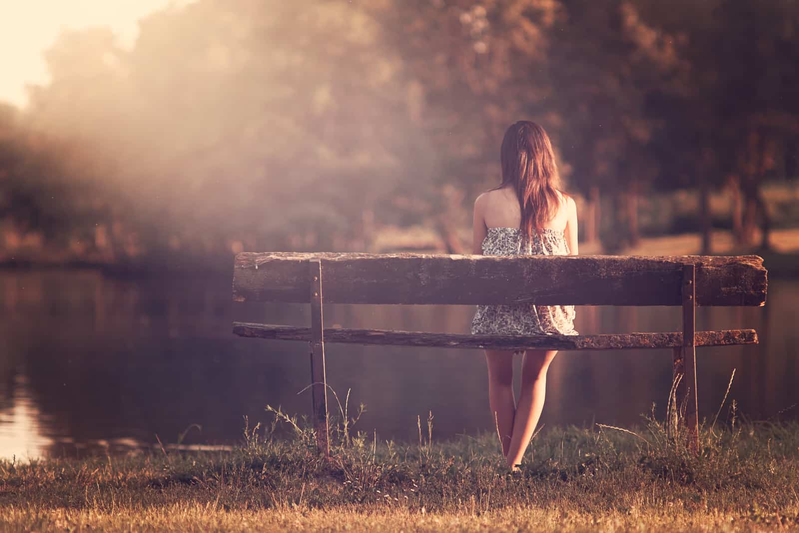 a sad woman sits on a bench with her back turned