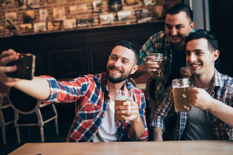 three male friends taking selfie while holding beer