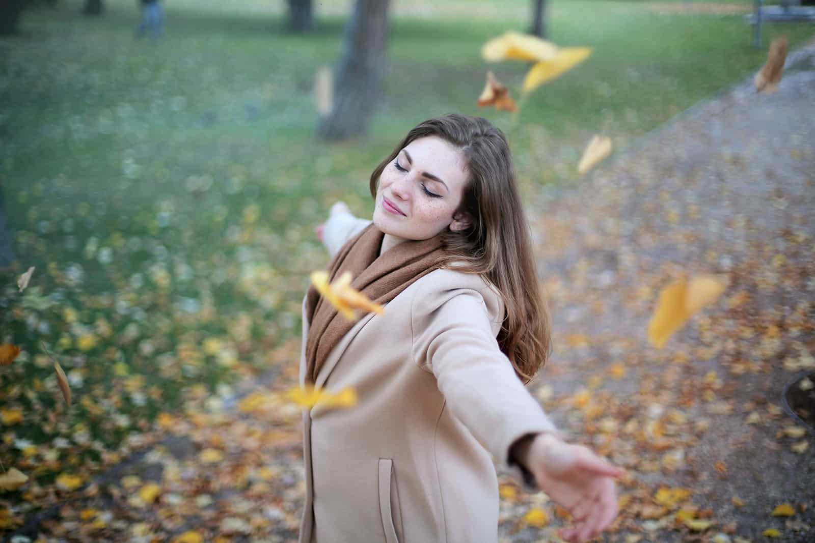 a calm woman standing under the falling leaves with eyes closed