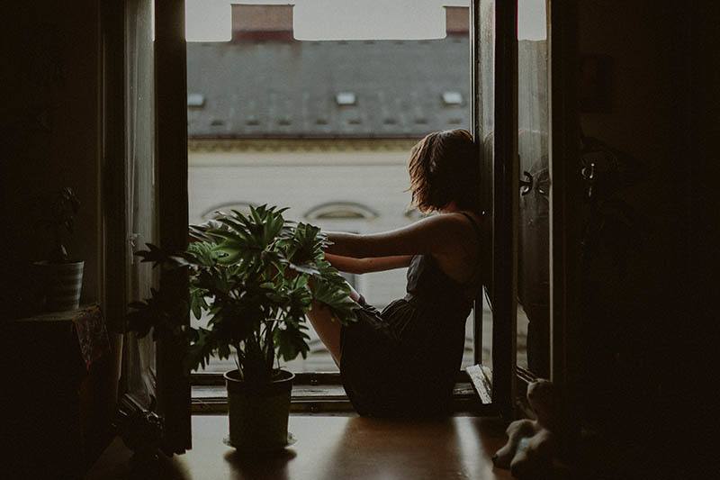 sad woman sitting by the window and plant