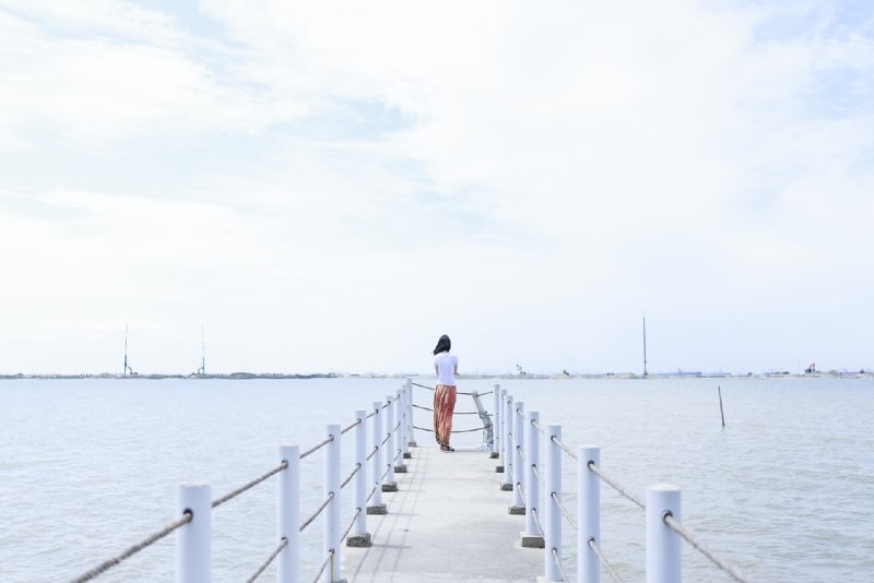 woman in white top standing on dock looking at water