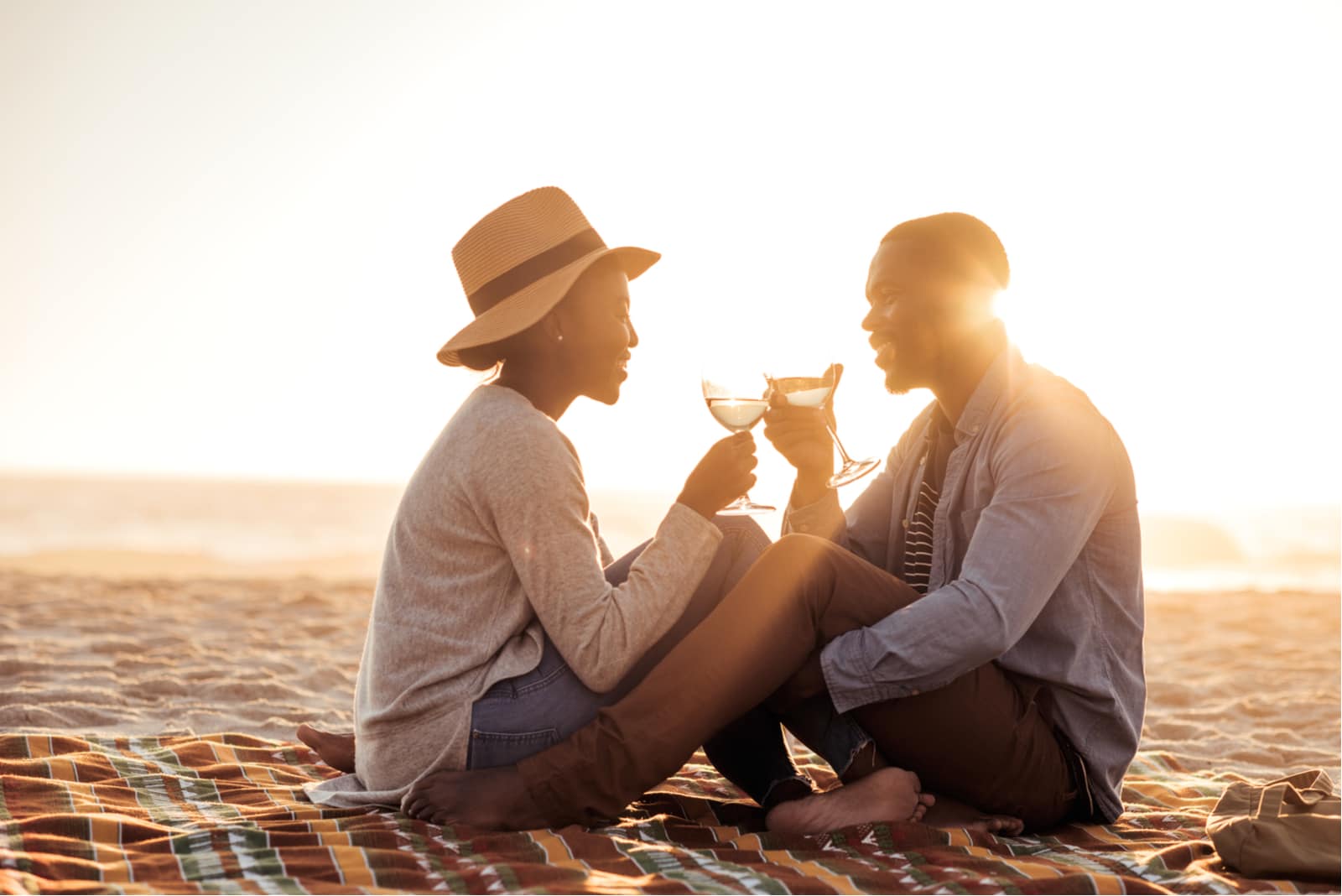 a romantic african american couple at sunset sitting on the beach drinking wine
