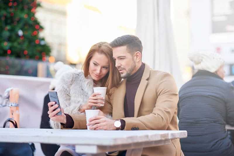 couple sitting in outdoor cafe and looking at smartphone